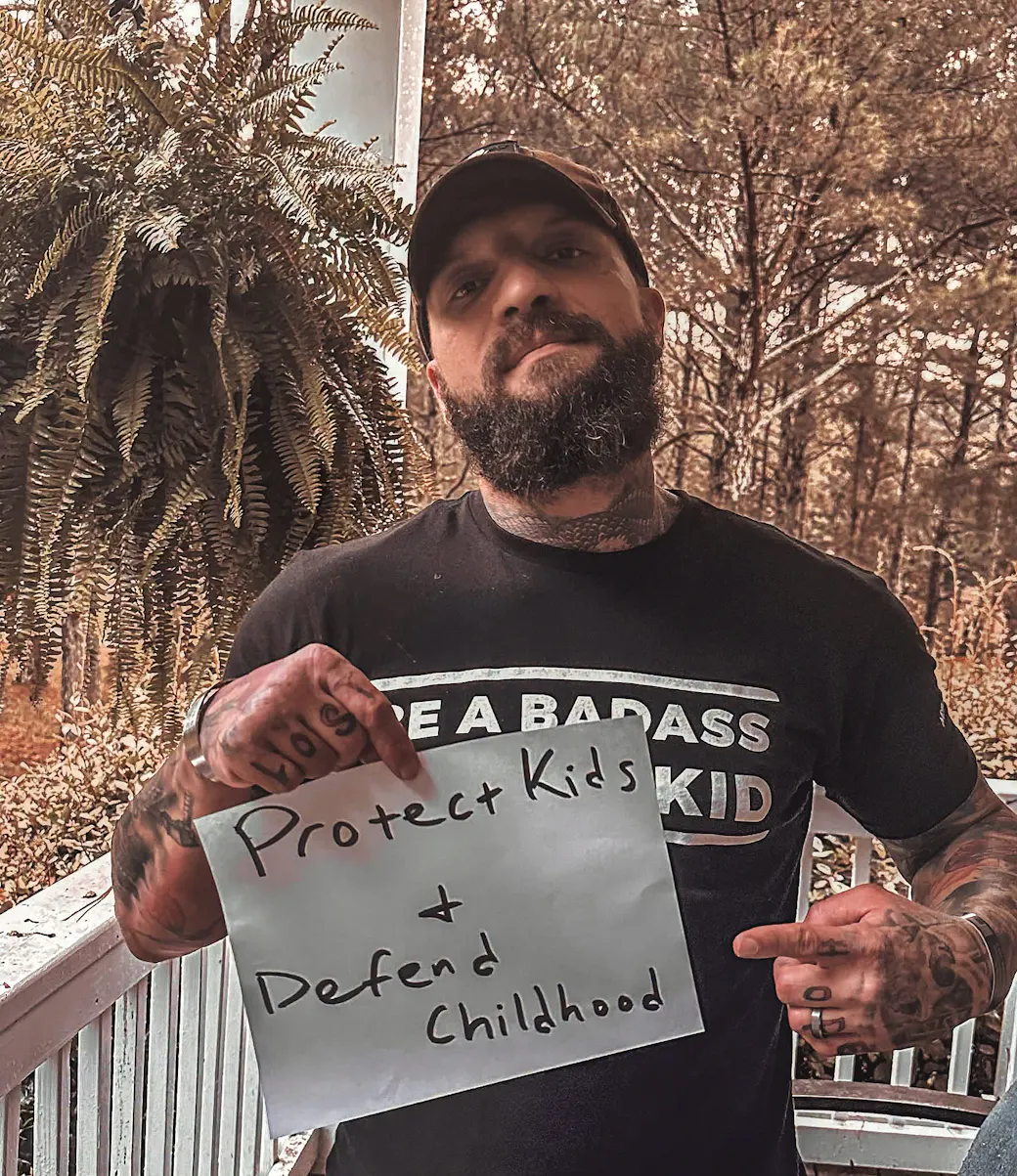 Ben Owen holding a handwritten sign that reads 'Protect Kids &amp; Defend Childhood'