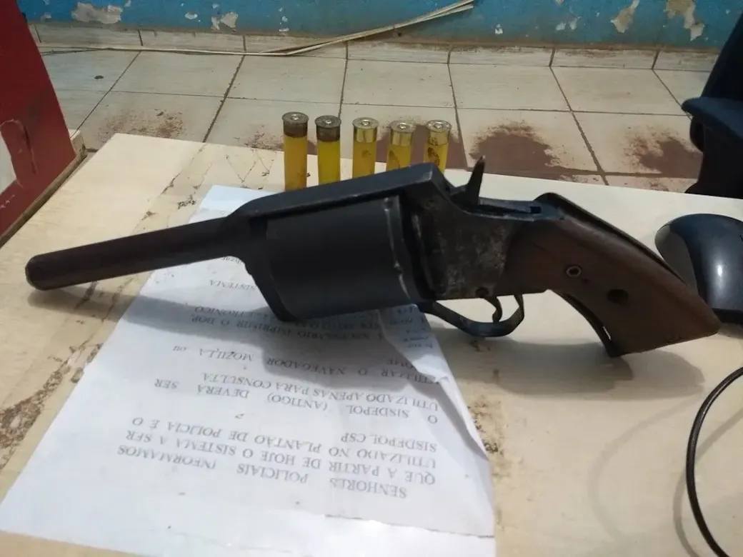 Handmade revolver-style pistol with a wooden grip and five shotgun shells on a police station desk in Brazil