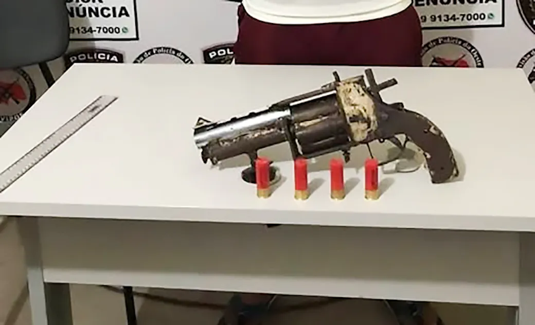 Rusted handmade revolver-style shotgun pistol on a police table next to four red shotgun shells