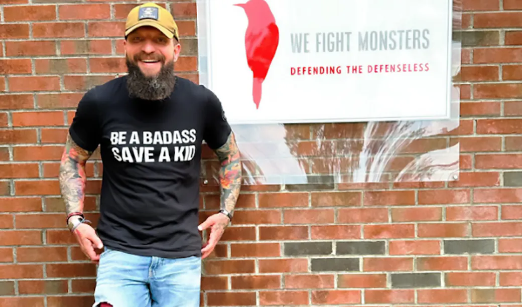 Ben Owen, co-founder of the counter-trafficking organization "We Fight Monsters." standing next to a WFM sign.